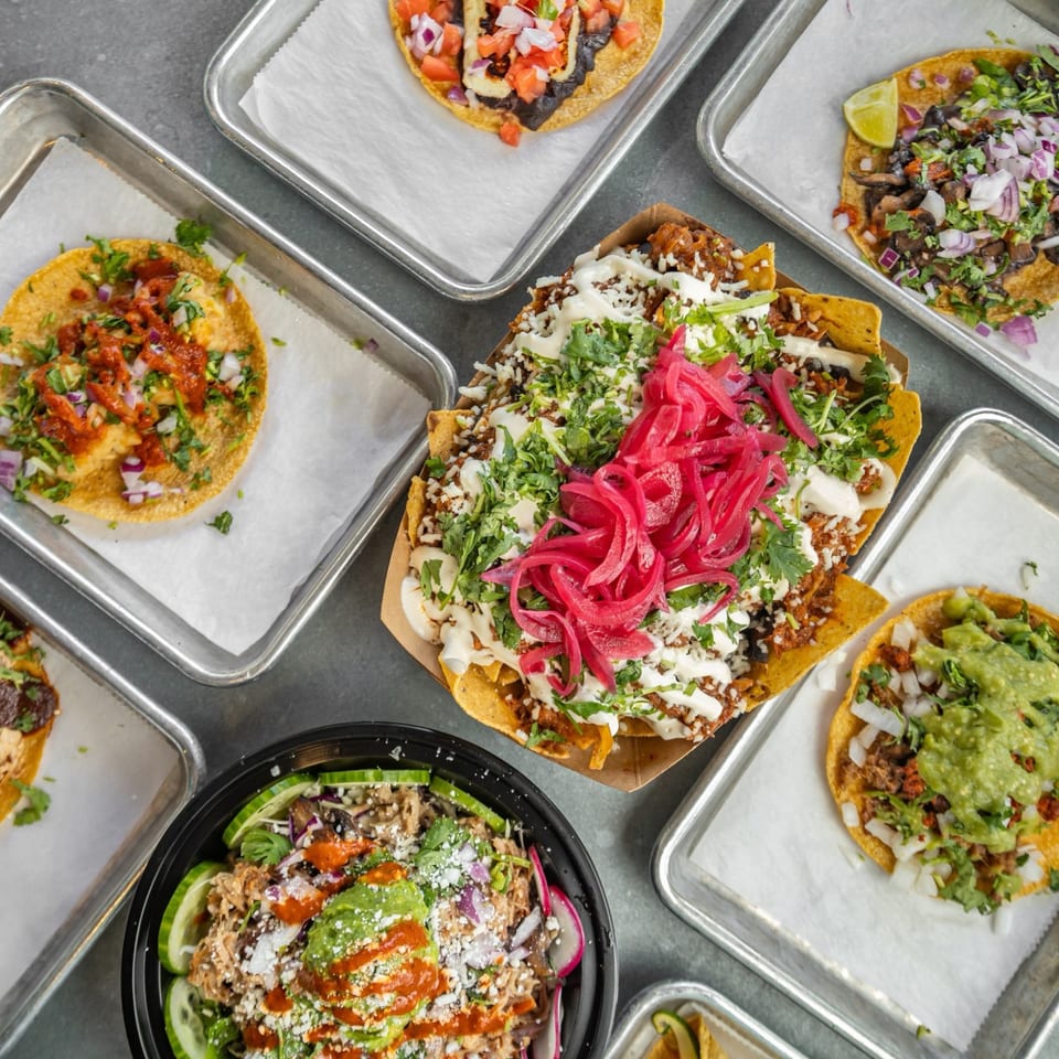 Overhead spread of colorful tacos, nachos and a bowl.