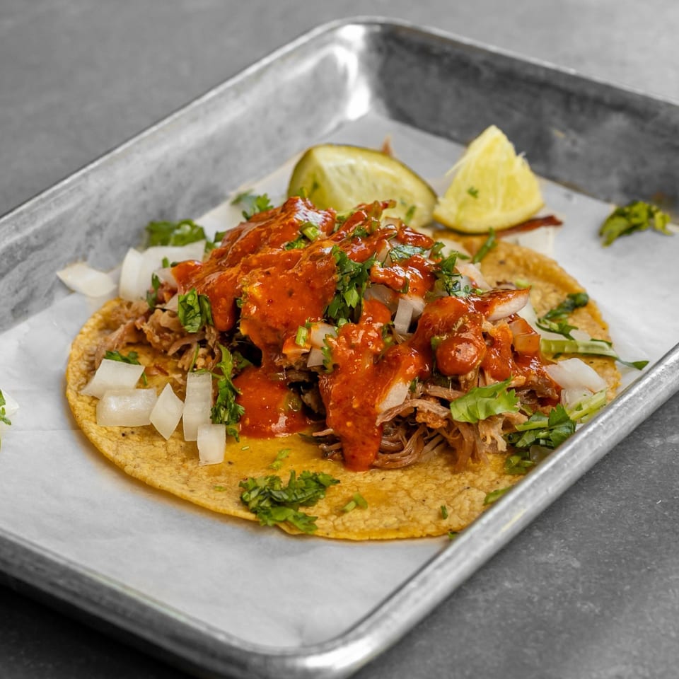 Taco topped with shredded meat, red salsa, onion and cilantro.