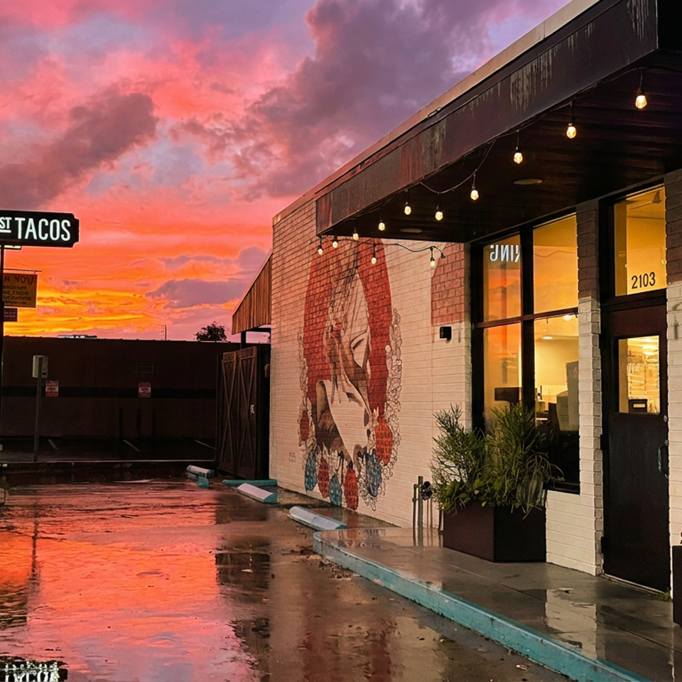 Hunger Street Tacos exterior at sunset, with a vibrant sky reflecting on the wet street.