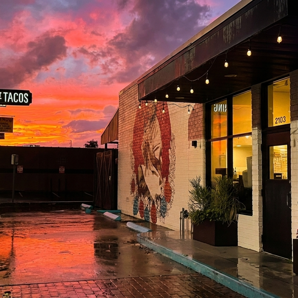 Hunger Street Tacos restaurant exterior at sunset, with a vibrant red and orange sky reflecting on wet pavement.